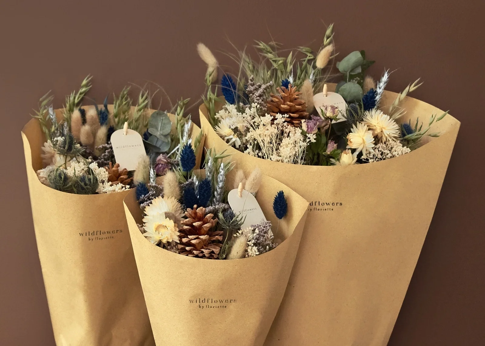 Dried flower bouquets with pinecones, blue phalaris, and strawflowers wrapped in kraft paper